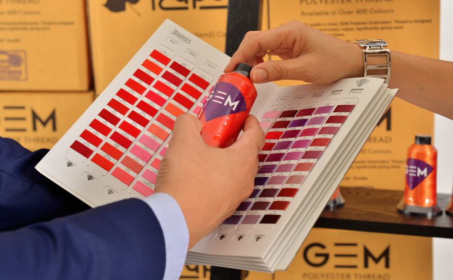 hand passing red cone of thread on colour chart catalog