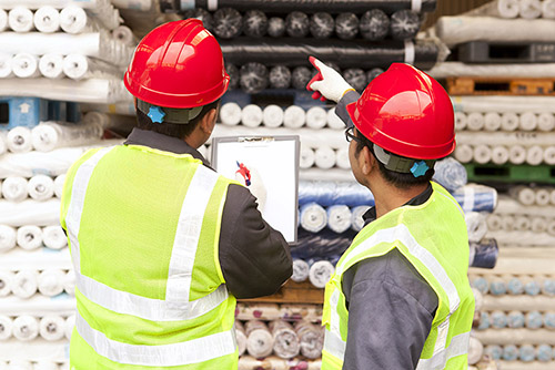 foto de perto de dois trabalhadores de controle de qualidade inspecionando rolos de tecido por trás